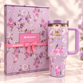 A lavender floral Stanley travel tumbler with a purple handle and lid, shown next to its matching floral gift box with a pink ribbon and visible Stanley branding.